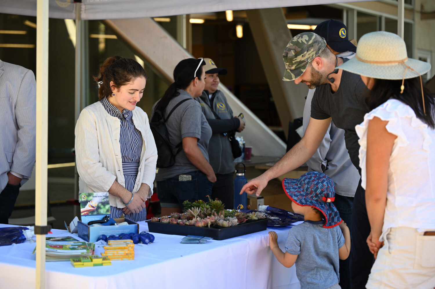 a person standing at a booth with succulents while an adult and child point at them